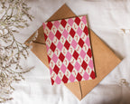 Red and pink patterned card with a brown envelope on a white fabric background
