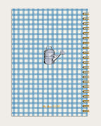 Notebook with blue and white checkered cover featuring a watering can illustration, on a light gray background.