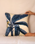 Decorative pillow with blue leaf pattern held by a hand against a beige background