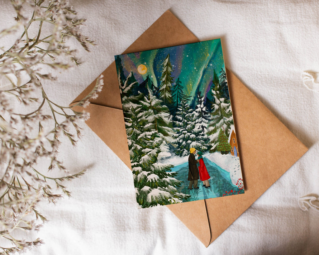 Greeting card with a winter scene of a couple  in a red coat standing in a snowy landscape, placed on a brown envelope with a white background.